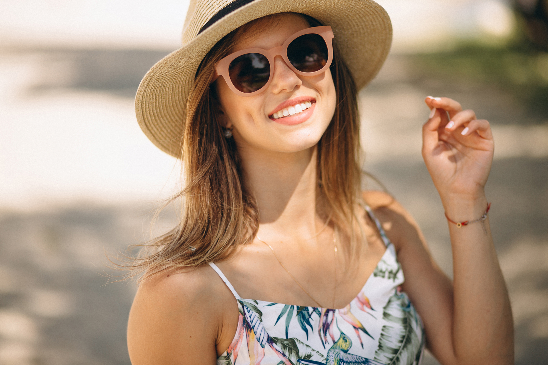 Woman with a hat and sunglasses smiling at the beach