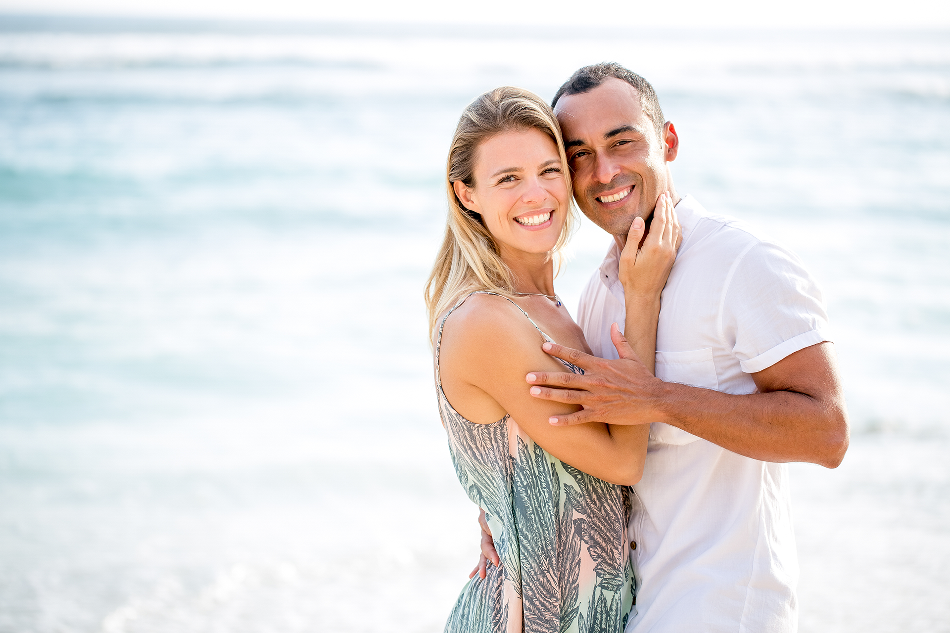 A man and woman embracing at the beach, both are smiling wide