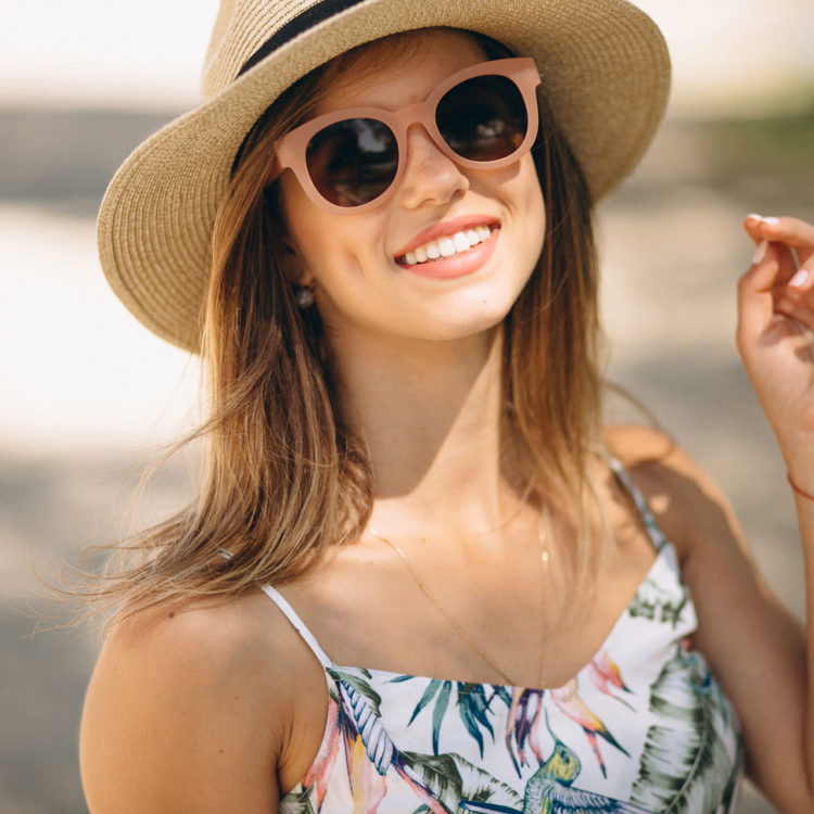 Woman with a hat and sunglasses smiling at the beach