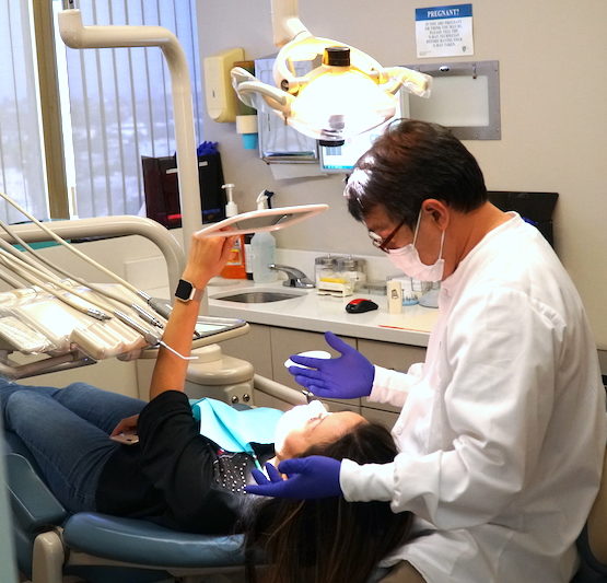 A patient lying on a table looking at her smile in a hand mirror with a dental assistant