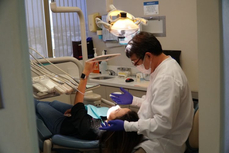 A patient lying on a table looking at her smile in a hand mirror with a dental assistant